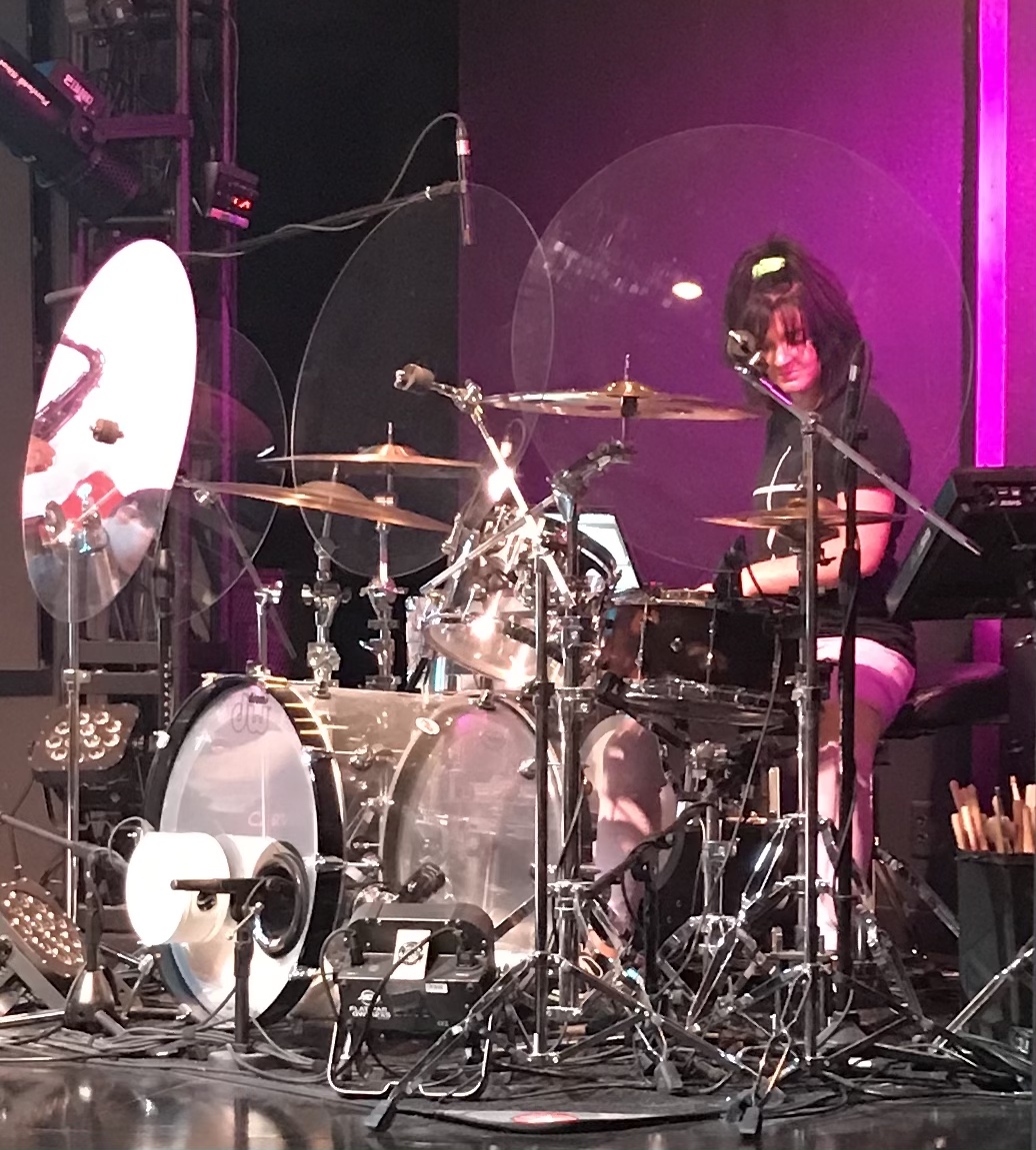 Brittany playing drums in a worship setting with purple stage light