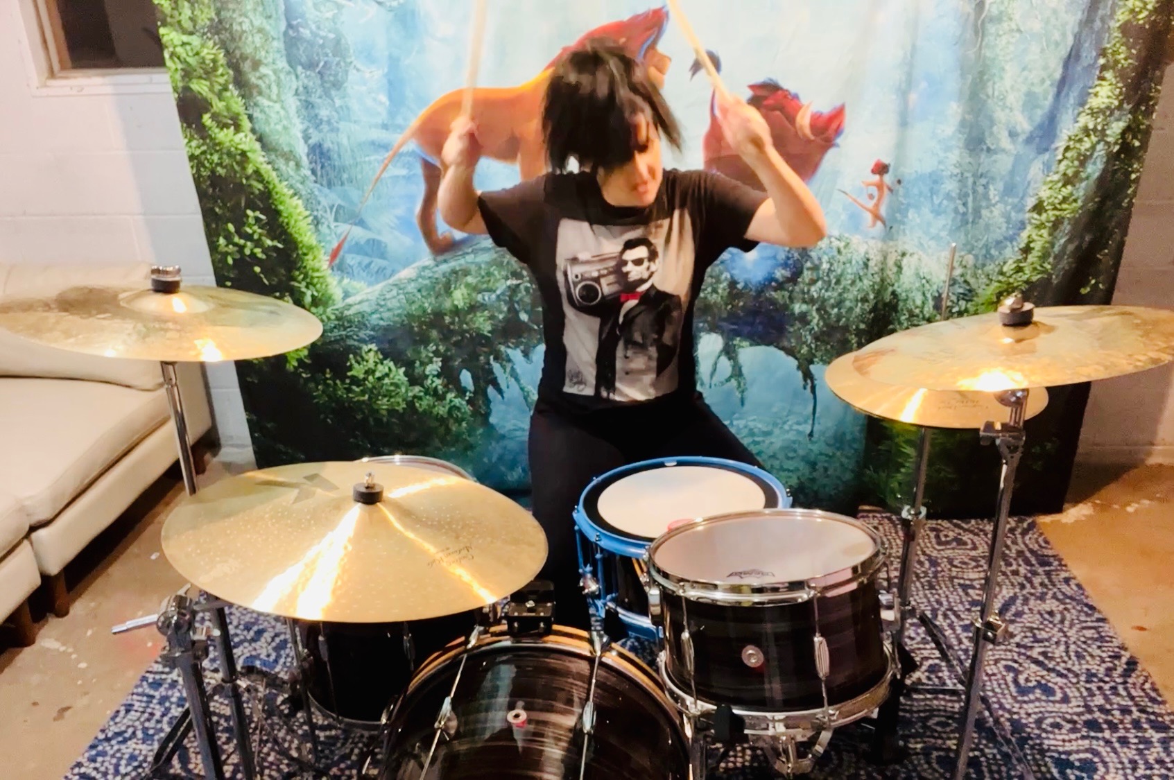 Brittany playing drums in front of a Lion King tapestry